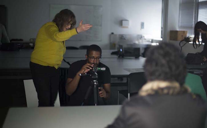 Student looking through camera with professor directing
