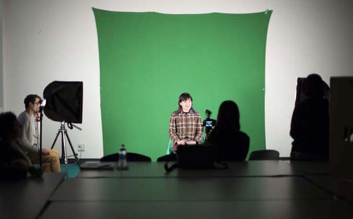 Student in front of green screen while other takes pictures