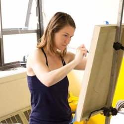 Student painting on canvas with window in background